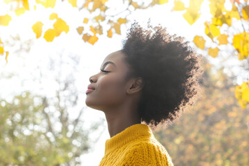 Wall Mural - African woman wearing yellow knitted sweatshirt in autumn park at sunny day