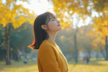 Wall Mural - Chinese woman wearing yellow knitted sweatshirt in autumn park at sunny day