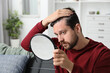 © New Africa - Man with hair loss problem looking at mirror indoors