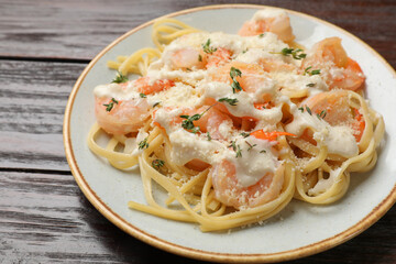 Tasty pasta with shrimps, creamy sauce and cheese on wooden table, closeup