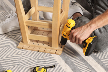 Poster - Man repairing wooden stool with electric screwdriver indoors, closeup