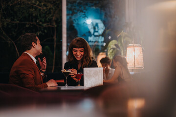 Wall Mural - A joyful couple shares an evening at a stylish restaurant, enjoying drinks and heartfelt conversation. Warm lighting creates a cozy and romantic atmosphere.