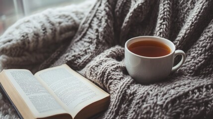 A cozy sweater draped over a chair next to a cup of tea and a book on a cold winter day.