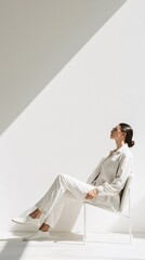 Poster - Person in neutral clothing sitting in a minimalist chair, side view, soft shadows.