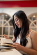 © bongkarn - An attractive Asian woman is focused on reading while working remotely from a coffee shop.