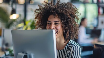 Poster - A woman with curly hair is sitting in front of a computer monitor and smiling