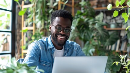 Poster - A man wearing glasses and a blue shirt is smiling while using a laptop