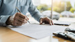 © Studios - Man signing car insurance document or lease paper. Writing signature on contract or agreement. Buying or selling new or used vehicles. Car keys on table. Warranty or guarantee. Customer or salesman.