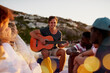 © StarDweller/peopleimages.com - Guitar, people and bonding together for break or social by beach on holiday, vacation or picnic. Friends, relax and fun with group for summer season, wellness and outdoor adventure by ocean in Greece