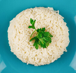 Steamed white rice lying on blue plate with parsley garnish