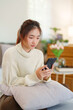 © Pichsakul - Young asian women in sweater enjoying with surfing entertainment on smartphone while sitting on comfortable couch to relaxation and doing activity for spending time with slow life lifestyle at home