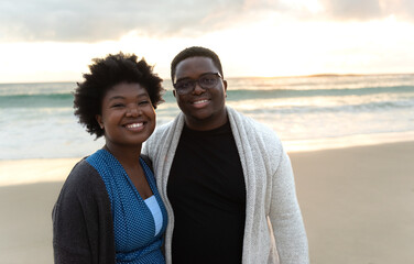 Young African couple smiling while standing on a beach at dusk