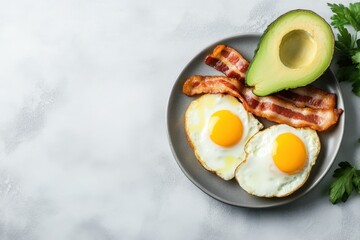 Delicious breakfast of sunny-side-up eggs, crispy bacon, and fresh avocado on gray plate