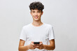 © SHOTPRIME STUDIO - Young man smiling while holding a smartphone in a plain studio background, showcasing modern technology engagement and casual lifestyle aesthetics