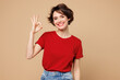 © ViDi Studio - Young smiling happy cheerful satisfied woman she wear red t-shirt casual clothes showing okay ok gesture look camera isolated on plain pastel light beige background studio portrait. Lifestyle concept.
