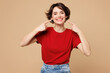 © ViDi Studio - Young smiling happy satisfied woman she wear red t-shirt casual clothes point index finger on white teeth look camera isolated on plain pastel light beige background studio portrait Lifestyle concept
