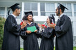 © Kawee - Group of diverse students celebrating college achievement outside campus.