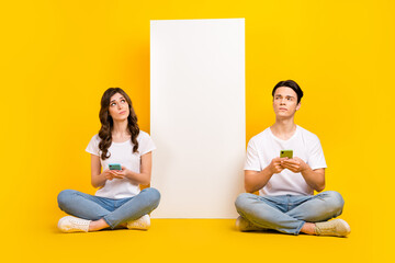 Wall Mural - Full length photo of funny unsure couple wear white t-shirts texting modern gadget empty space isolated yellow color background