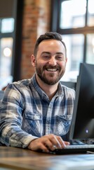 Fototapete - A man is smiling and sitting in front of a computer