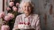 © Karen - Elderly woman holding a cake with flowers in the background