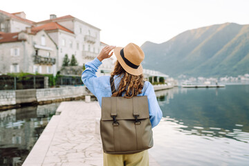 A young woman traveler enjoys the serene waterfront view in a coastal village during sunset time. Back view. Europe travel. Lifestyle, vacation, tourism, nature, active life.