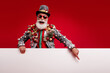 © deagreez - Photo of happy cheerful old man point white empty space wear christmas tree balls costume sunglasses isolated red color background