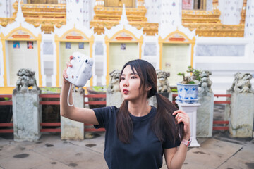 The group of South Asian tourists holding a map and searching for directions, with the iconic Wat Phra Kaew temple in the background in Bangkok, Thailand, enjoying their holiday adventure.