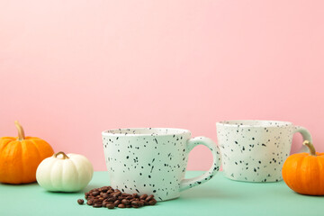 Coffee beans in white cups with pumpkins on pink background. Top view