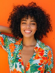 Wall Mural - Smiling young woman posing against a bright orange background. She is wearing a tropical floral print top.