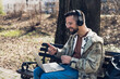 © Srdjan - Young hipster expatriate freelance worker man sitting in park with laptop and wireless headphones having business video call with client. Male IT engineer with cool attitude online work telecommuting.