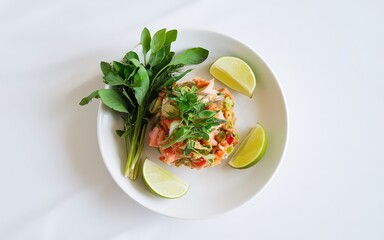 Spicy salmon salad with lime wedges and fresh herbs on a white plate.