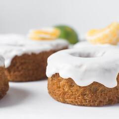 Wall Mural - Iced mini bundt cake on a white tray, vanilla bundlette cakeswith a clementine segment on a white background, small vanilla bundt cakes with an icing glaze