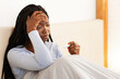 © Prostock-studio - Fever And Headache. Sick African American Lady Holding Thermometer Touching Head Sitting In Bed At Home.