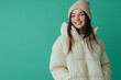 © Farid - Photo of a cheerful young woman wearing an oversized puffer jacket and beanie, isolated on a pastel green background