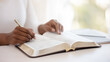 © Kateryna - A serene scene of a personâs hands carefully flipping through the pages of the Bible during a morning study session at home. A notebook and pen sit beside the open Bible, suggestin