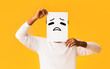 © Prostock-studio - Black man putting peace of paper with sad emoji over his face, orange background