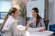 © Wasana - Two women are sitting at a desk, one of them holding a piece of paper
