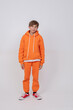 © Светлана Лазаренко - Teenage boy in orange clothes stands on a white background. He is wearing a tracksuit and red sneakers.
