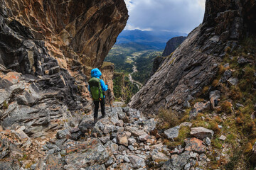 Woman backpacker climbing up on steep cliff edge at high altitude mountains top