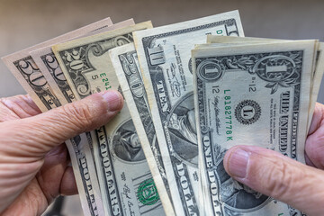 Close-up of a man counting US dollars banknotes on his hands, against plain background. One, ten, twenty and fifty dollar denominations.