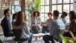 © sakir - Corporate business team meeting with a manager or coach. Group of happy diverse, multiracial people sitting in a circle around a standing woman in an office. generative ai.