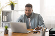 © Prostock-studio - Young black businessman using laptop and taking notes at worklace in modern office,free space