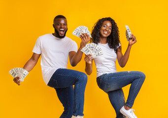 African american cheerful couple dancing with money in their hands, lifting legs up