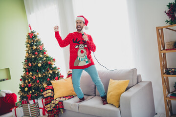 Poster - Full size photo of nice young man raise fist sing mic sofa ugly sweater christmas time apartment indoors