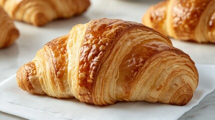 A close-up of a croissant flaky crust and golden color, placed on a white napkin with a light background, showcasing its freshly baked appeal.