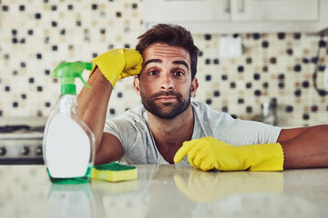 Cleaning, tired and portrait of man by kitchen counter in home for sanitizing germs, bacteria or dirt. Gloves, housekeeping and person with fatigue for hygiene with table for dust in apartment.