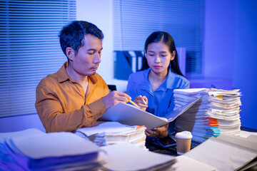 Image of businessman working hard in front of many documents on desk at office late at night with serious action. Concept of working hard and too late.