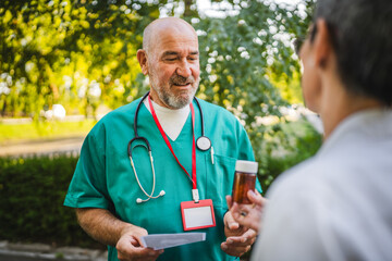 Two man and woman senior mature doctors discuss prescription outdoor