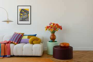 Minimalist living room with a cozy white sofa, colorful throw pillows, and bold flower arrangements. Abstract wall art and vibrant decor create a playful yet modern aesthetic.