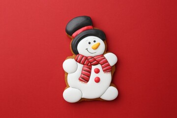 Poster - Tasty Christmas cookie in shape of snowman on red background, top view